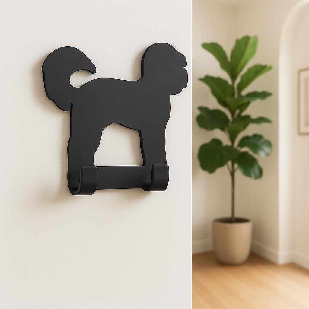 Black dog-shaped wall hook on a white wall with a plant in the background.