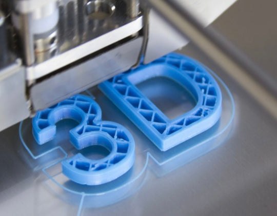 3D printer in action with blue 3D-printed letters on a metallic surface
