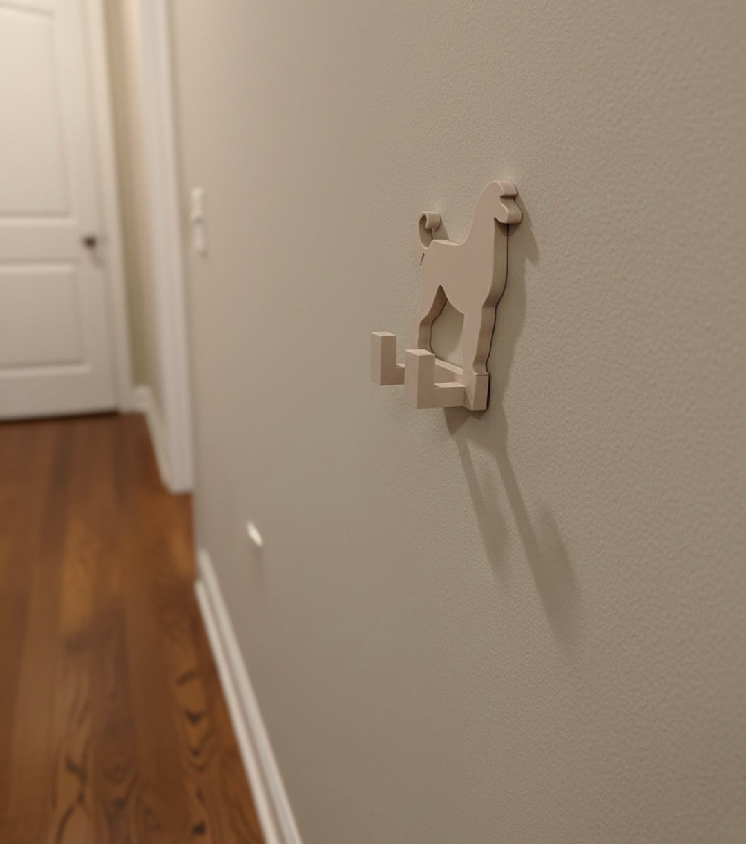 Side view of a 3D printed Afghan Hound dog wall hook mounted on a hallway wall, showing depth and hook profile in a home interior.