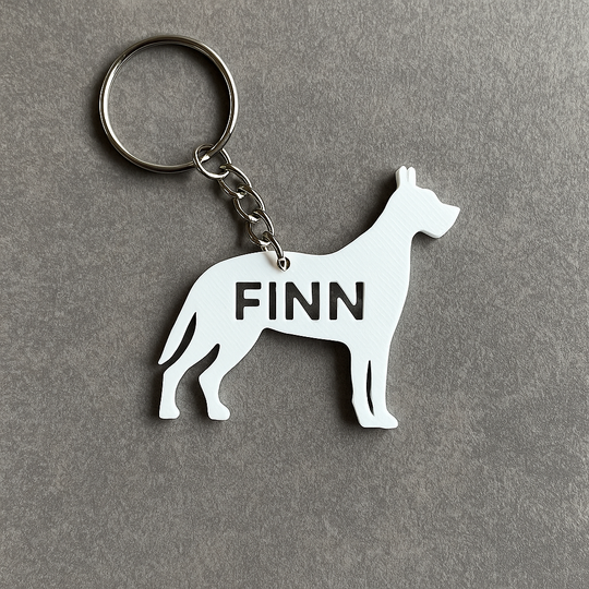 White 3D-printed Great Dane-shaped keyring personalized with the name 'Finn'. Attached to a silver., shown on grey background. Minimalist custom pet accessory for dog lovers.
